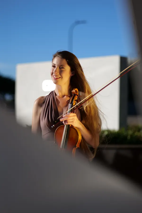 Madalyn playing violin outdoors at dusk, smiling mid-phrase