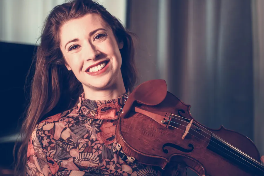 Smiling warmly with violin held up, floral blouse