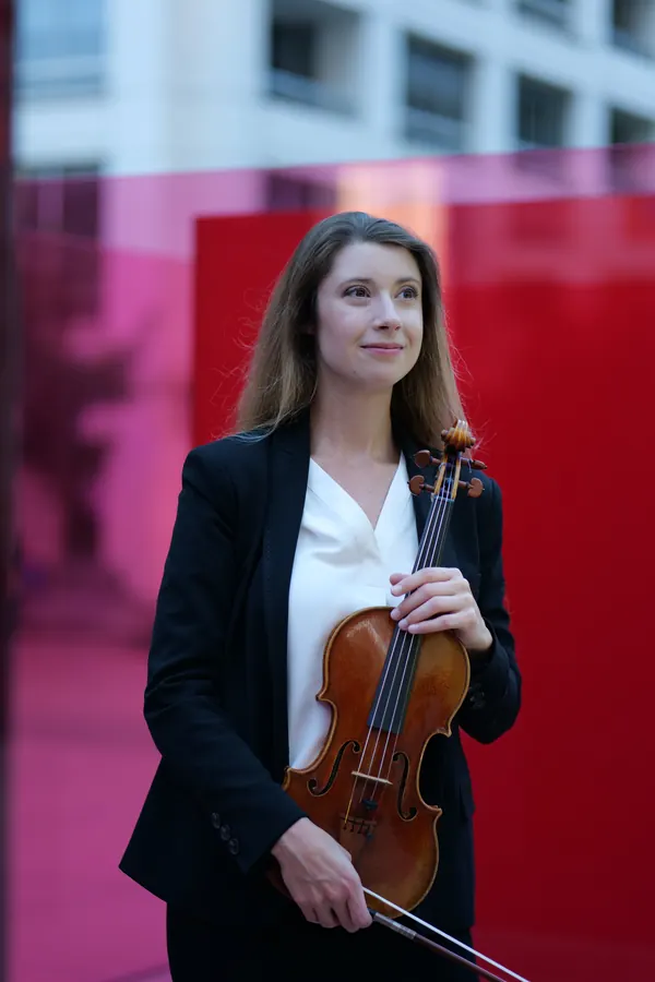 Bright smile with violin, red glass backdrop — photo by Cicely Parnas